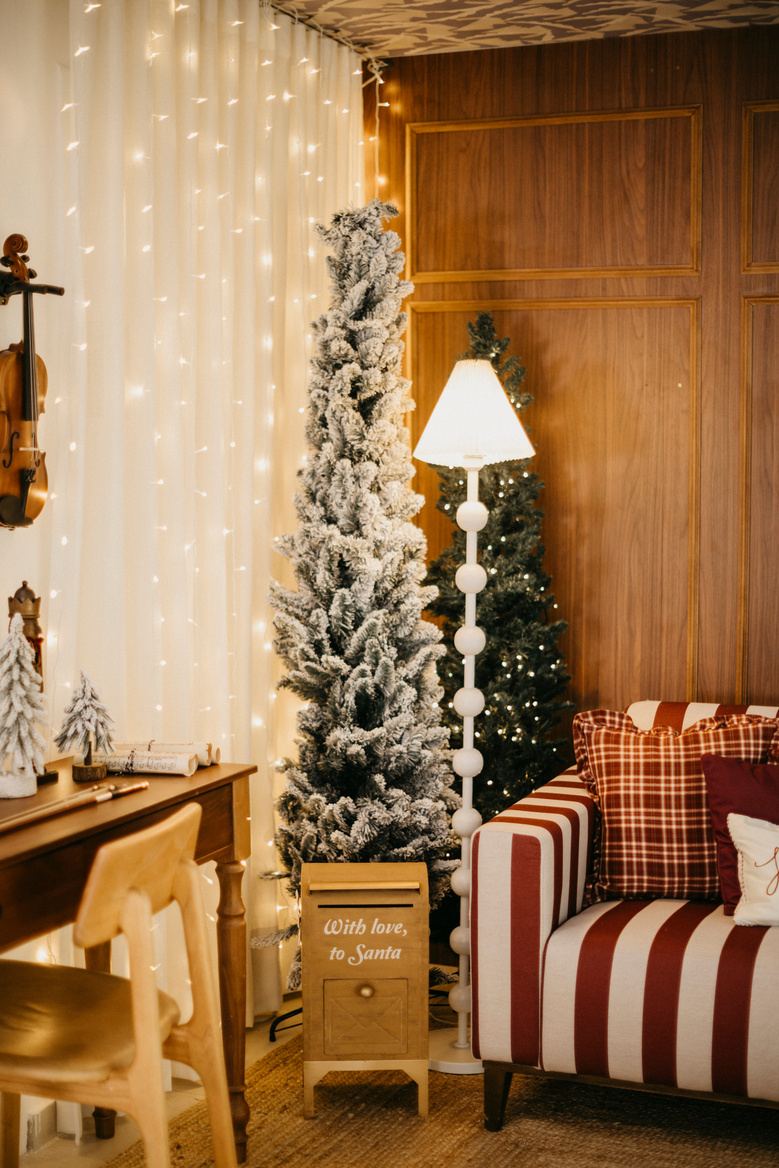 Árvore de Natal nevada, luminária e escrivaninha de madeira com cortinas iluminadas