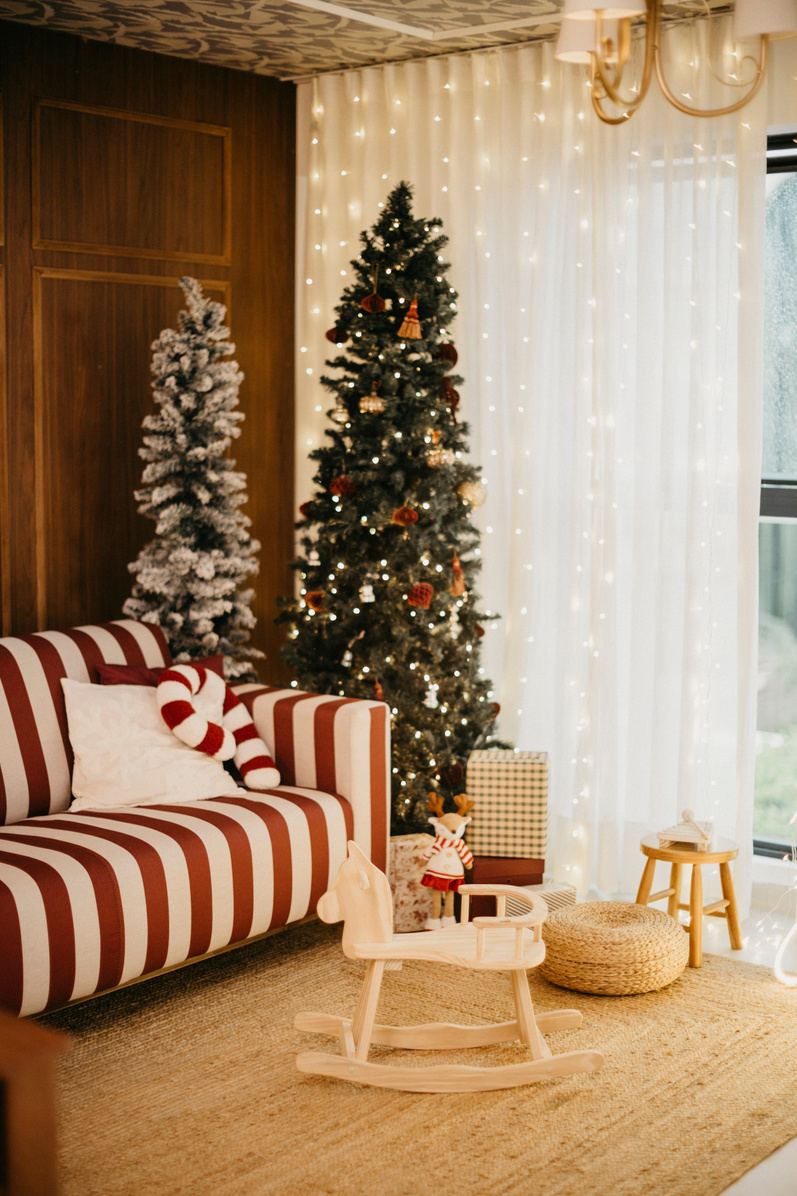 Sofá listrado vermelho e branco ao lado de árvores de Natal iluminadas e cortinas de luzes